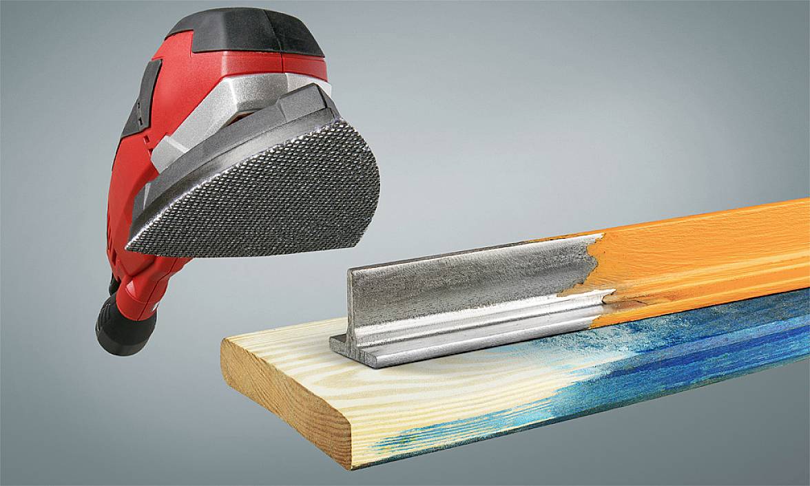 A red sanding machine is working on the edge of a wooden beam. The beam is partially painted blue. An angle guide for chamfering lies nearby.