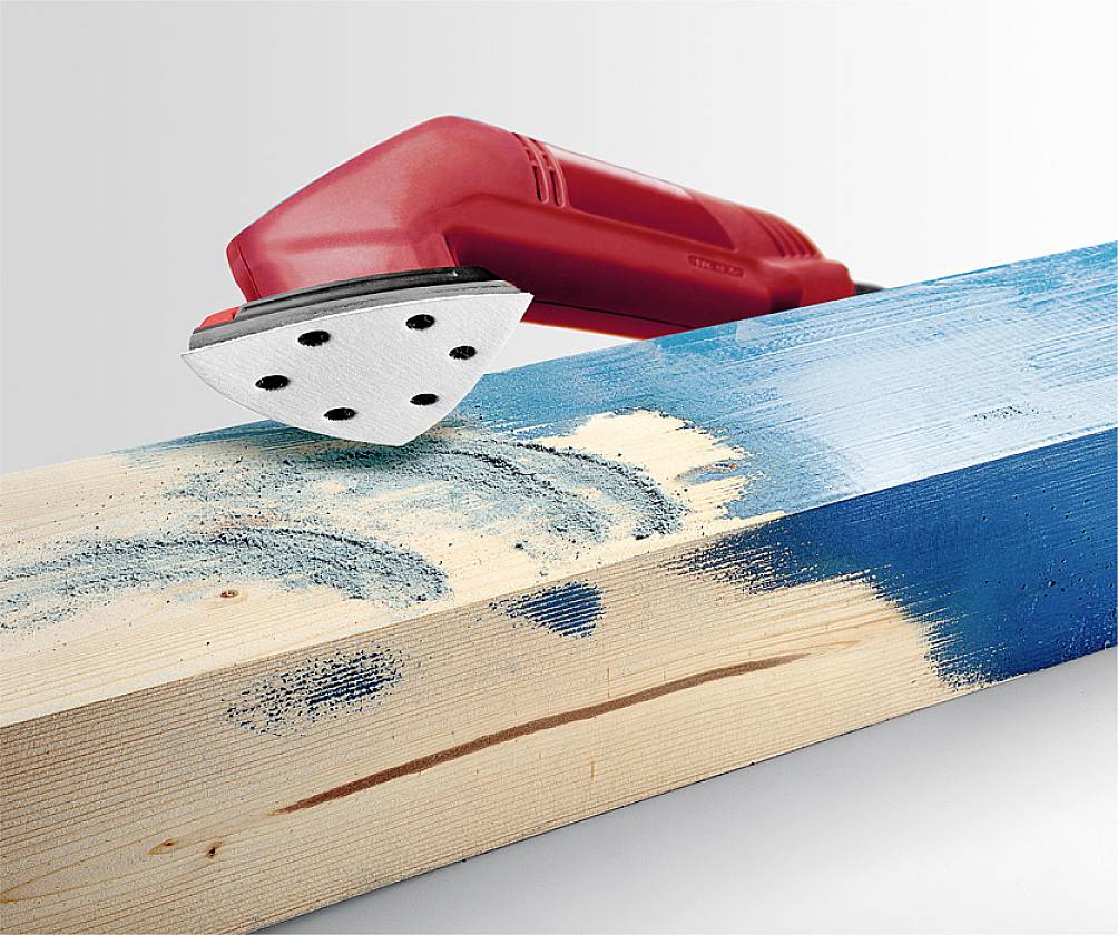 A red sanding tool smooths the blue paint on a wooden beam, with parts of the wood grain showing through.