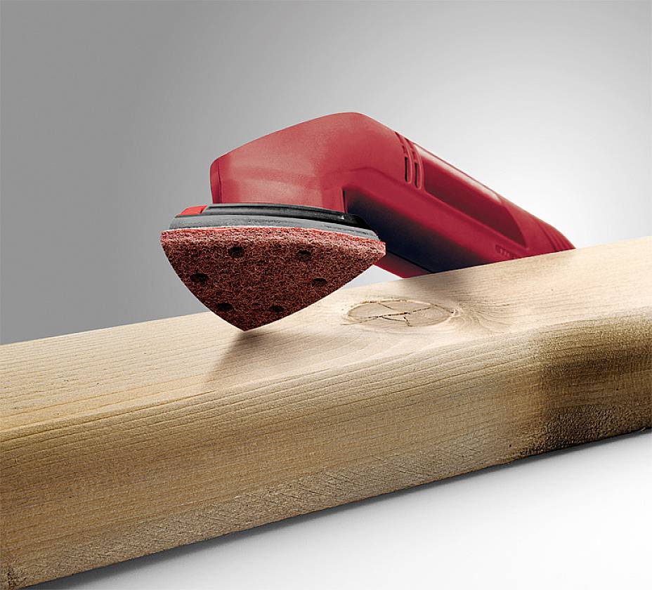 A red electric grinding tool is working on a piece of wood with a visible knot to smooth the surface.