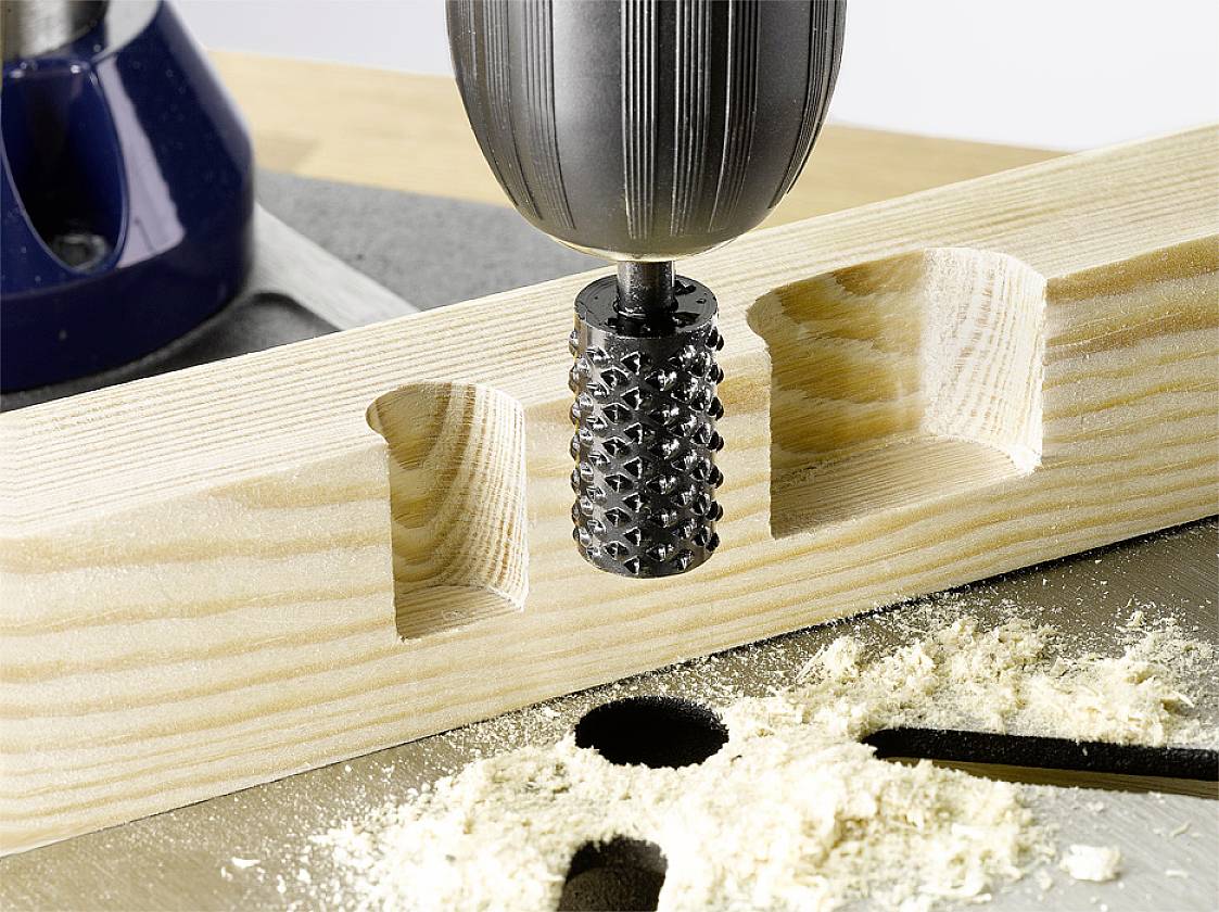 A drill bit is machining a piece of wood, creating wood shavings and recesses in various shapes, focusing on precise craftsmanship.