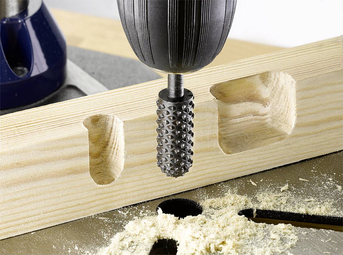 A milling machine precisely creates rectangular recesses in a piece of wood, surrounded by wood shavings.