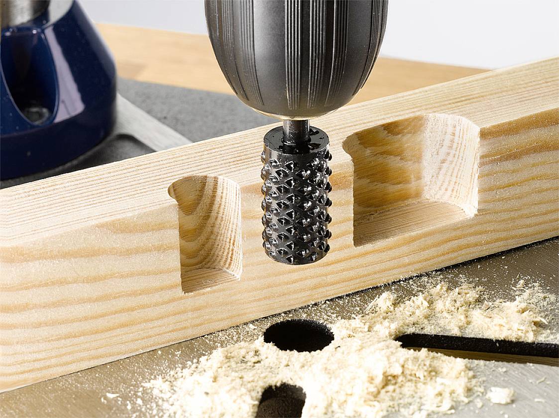 A router precisely drills intricate shapes into a piece of wood. Sawdust lies on the work surface. The main focus is on manufacturing the wooden forms.