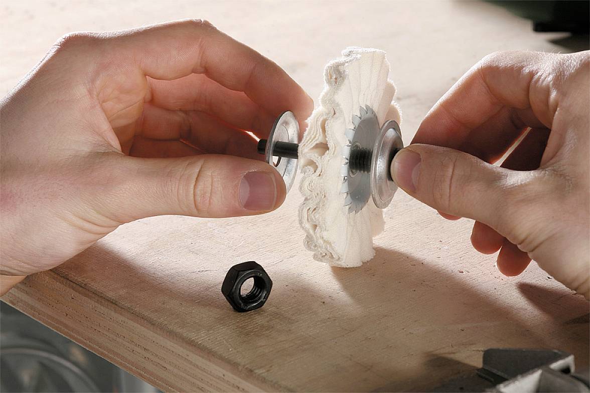Two hands are assembling a wooden gear wheel with metal components on a workbench. A hexagonal nut is lying beside it.