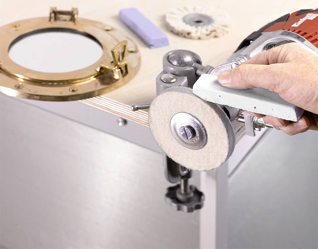A hand is polishing a round metal object with a polishing machine. Additional accessories are lying on the table.