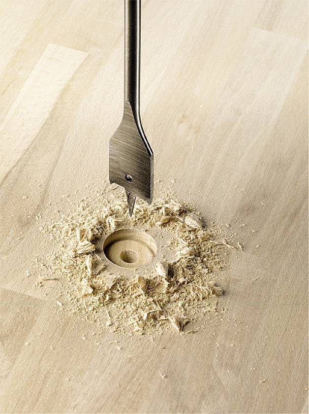 A drill is drilling a hole in light-coloured wood, surrounded by wood shavings.