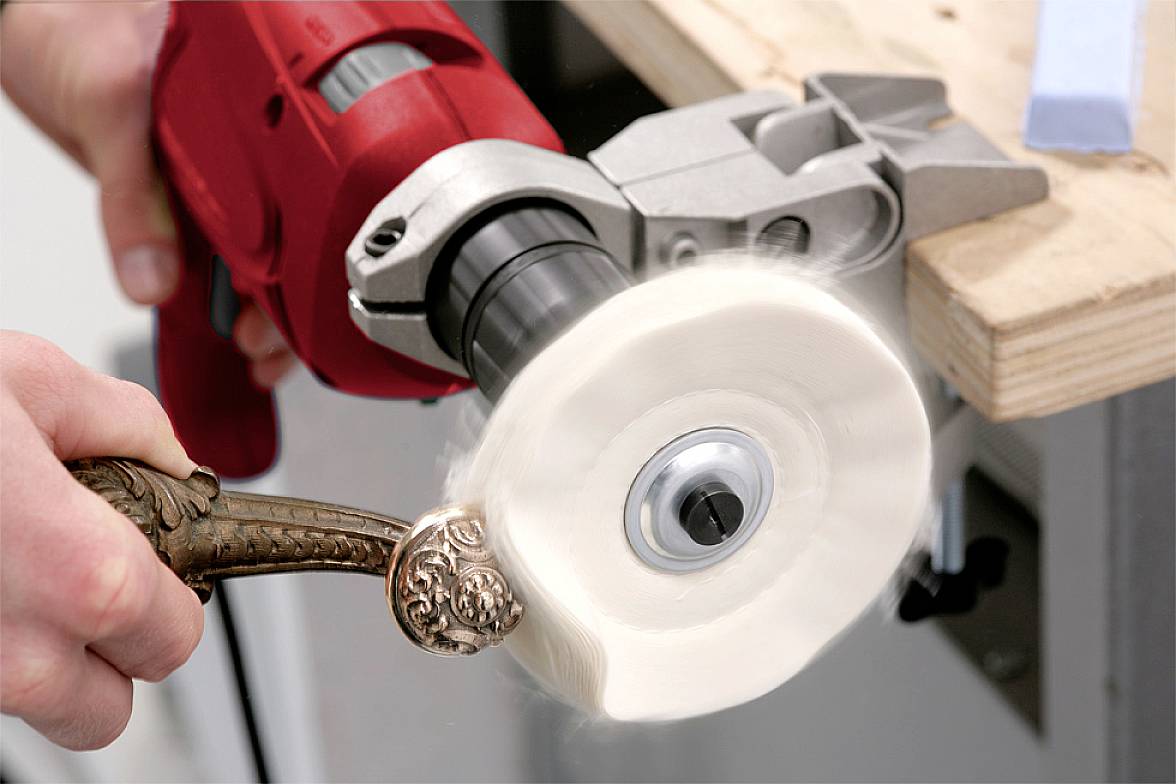 A person is polishing a silver candlestick with a rotating polishing disc attached to an electric tool.