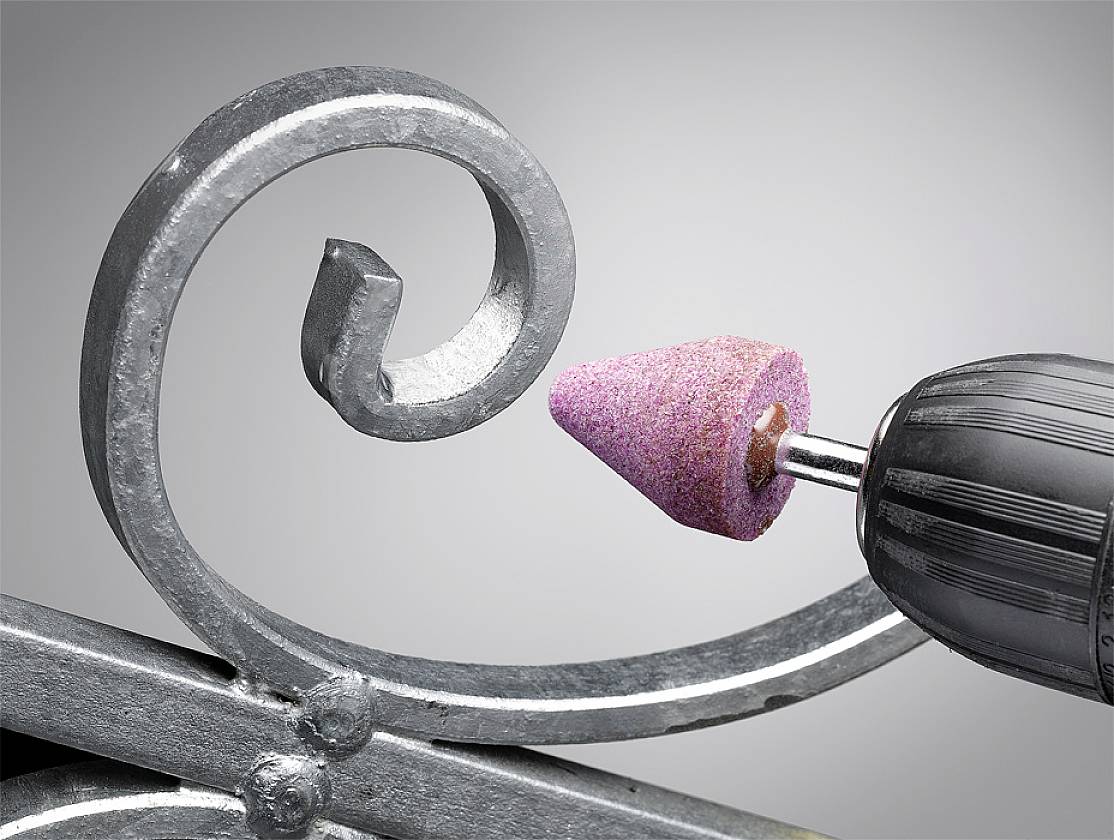 A metallic drill with a pink grinding attachment is machining a decorative metal piece, demonstrating precise craftsmanship and detailed processing.