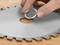 A hand places a silver metal ring into the central hole of a circular saw blade on a wooden surface.
