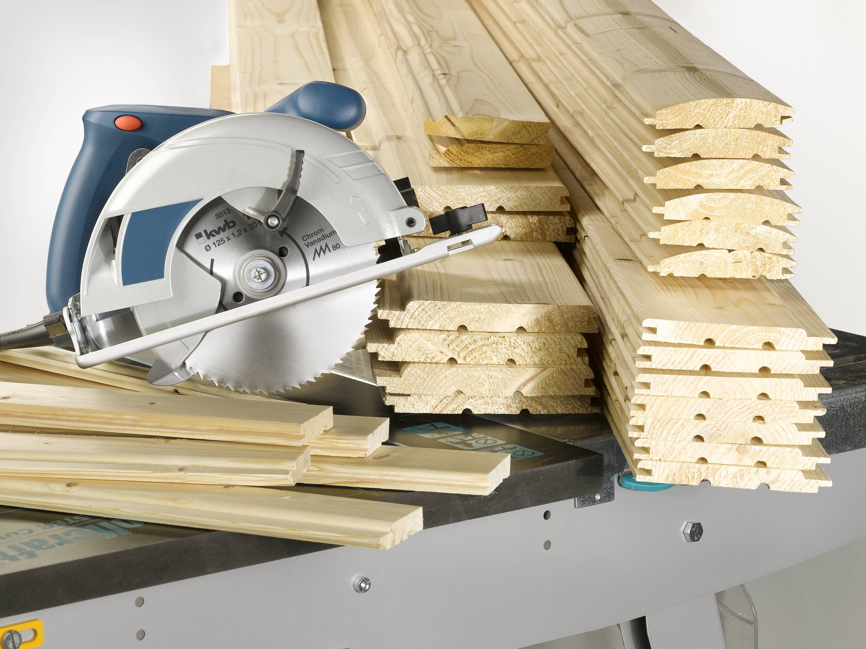 A circular hand saw is lying on a table next to several stacked wooden boards. It is apparently being used for woodworking.