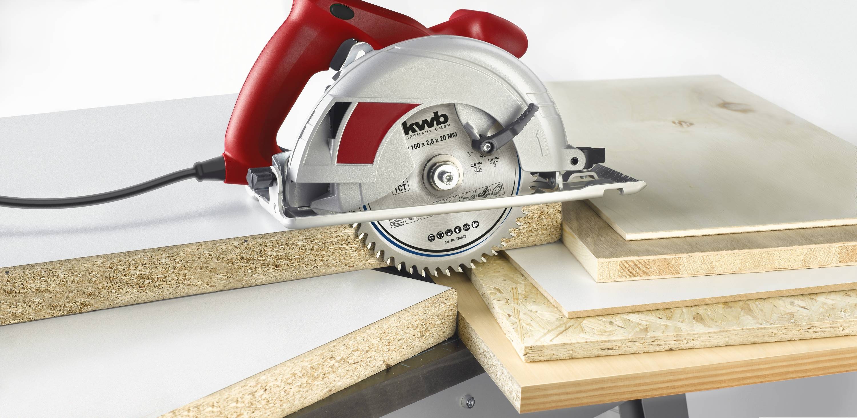 A circular saw with a red handle is cutting wooden boards of varying thickness and material on a table.