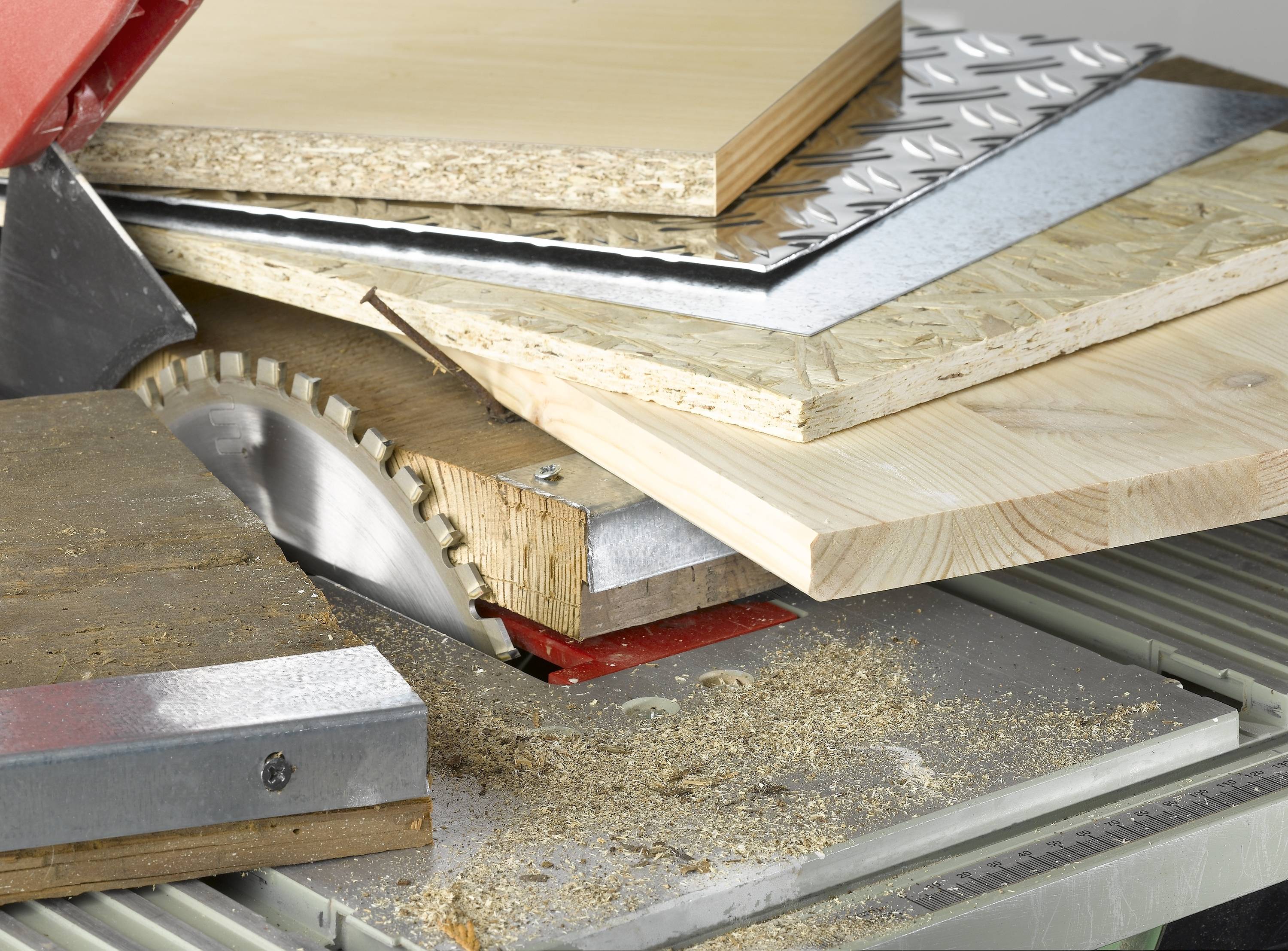 Various wooden and metal plates are being cut with a circular saw. Sawdust can be seen on the table.