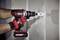 A person is using a red drill to bore a hole in a white wall. Protective gloves are being worn.