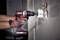 A man is using a cordless drill to make a circular hole in a wall. Cables are protruding from the wall opening.