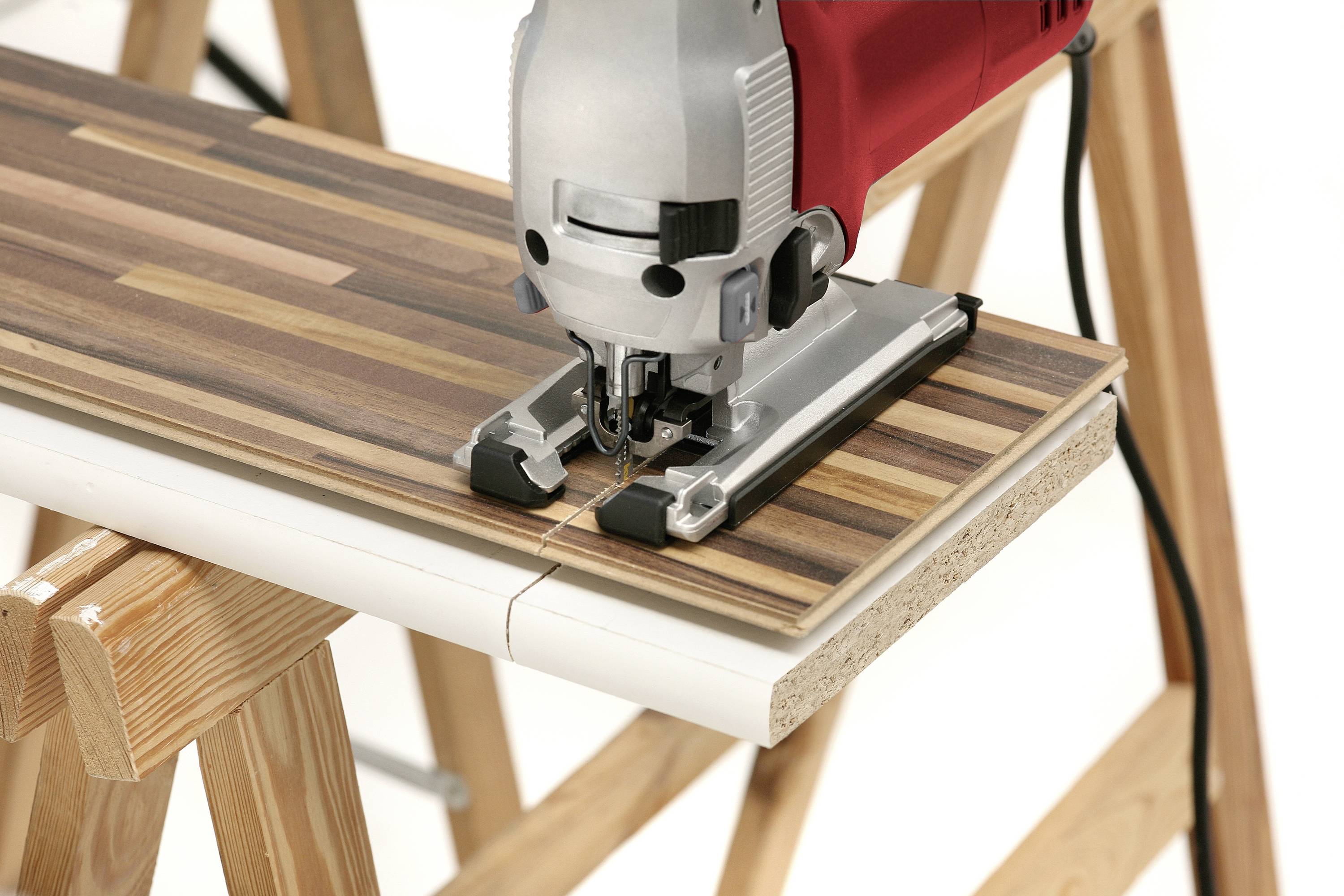 A red jigsaw cuts a wooden board on a workbench.