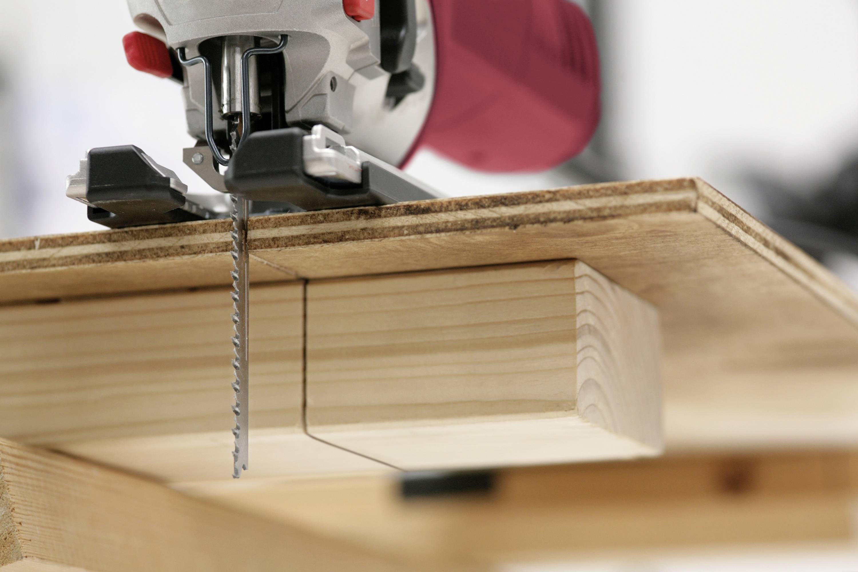 A woodworking tool is cutting through a wooden board, using a guide rail for a precise, straight cut.