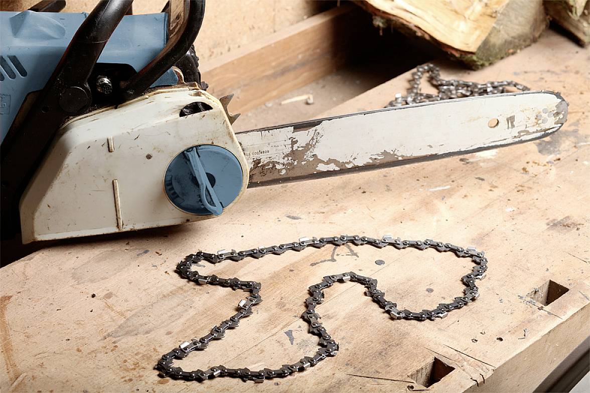 Petrol-powered chainsaw on a wooden surface, with the saw chain laid beside it.