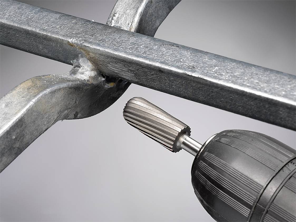 Drill processes metal, showing a close-up of a rotating grinding attachment on a steel beam, with sparks lightly spraying.