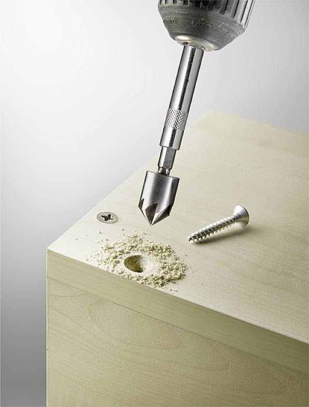 A screwdriver drills a hole in a wooden board. A screw and wood shavings lie beside it.