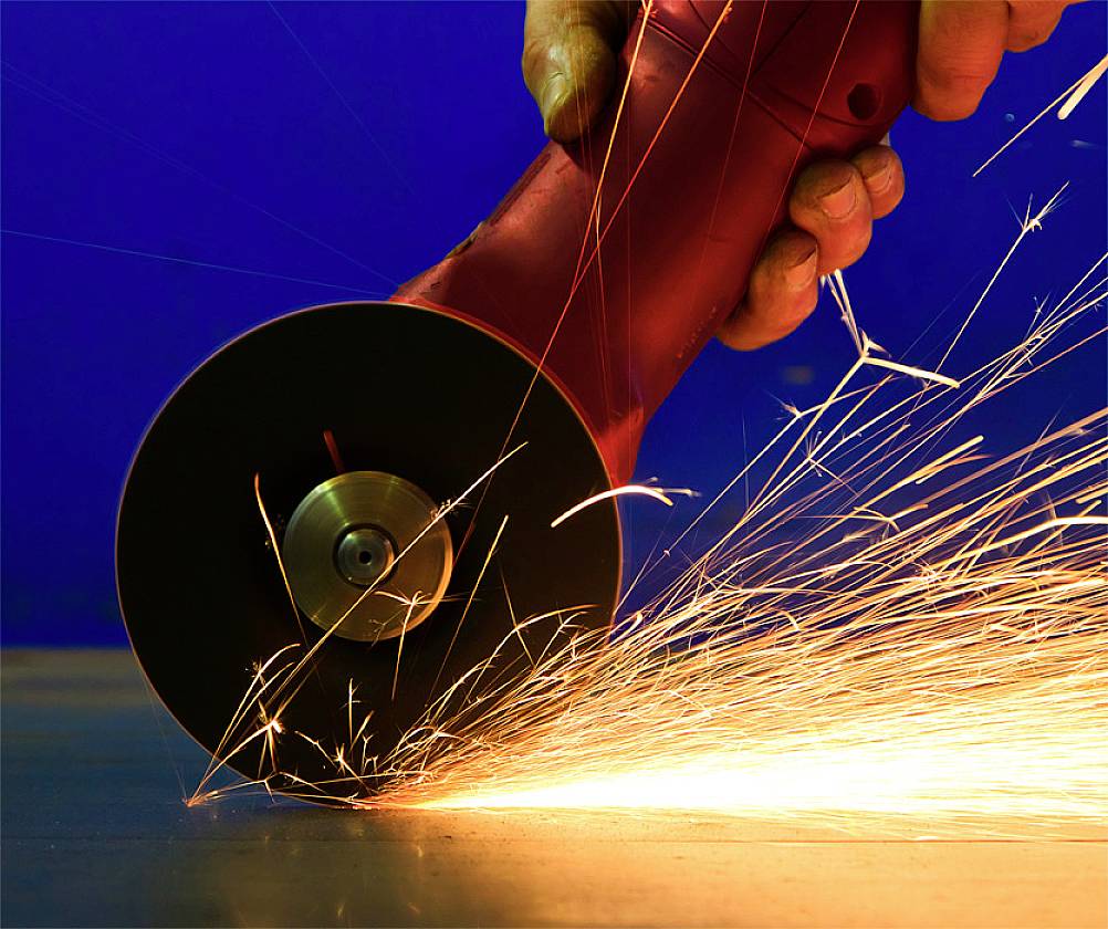 A hand is using an angle grinder, creating sparks on a metal surface.