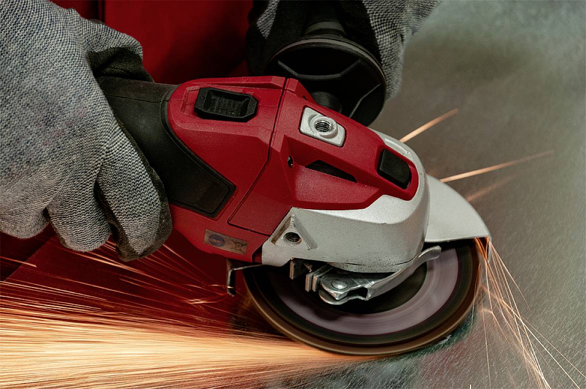 A person is wearing safety gloves and working with an angle grinder while sparks are flying.
