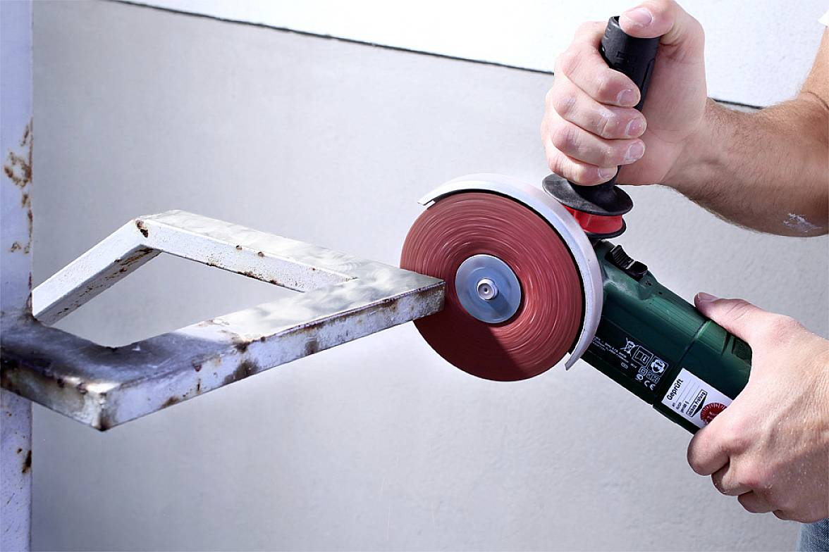 A person is cutting a piece of metal with an angle grinder. The grinding head is spinning rapidly, sparks are not flying.