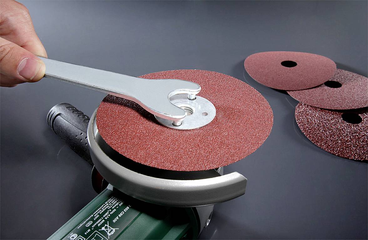 A person is securing a grinding disc to an angle grinder using a spanner. Additional grinding discs are lying nearby.