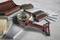 An angle grinder is lying on a concrete surface, surrounded by bricks, ceramic tiles, roof tiles, and granite slabs.