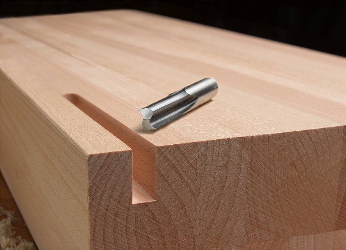 Wooden board with a milled recess, with a metal milling cutter placed on top.