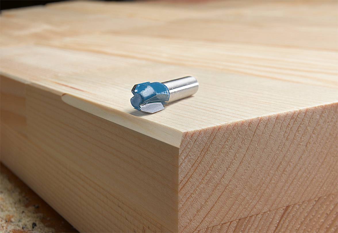 A drill bit is lying on a stack of wood with a smooth surface, ideal for woodworking or wood project designs.