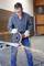 A person is wearing safety glasses and gloves while cutting a metal pipe with an angle grinder. Sparks are flying.