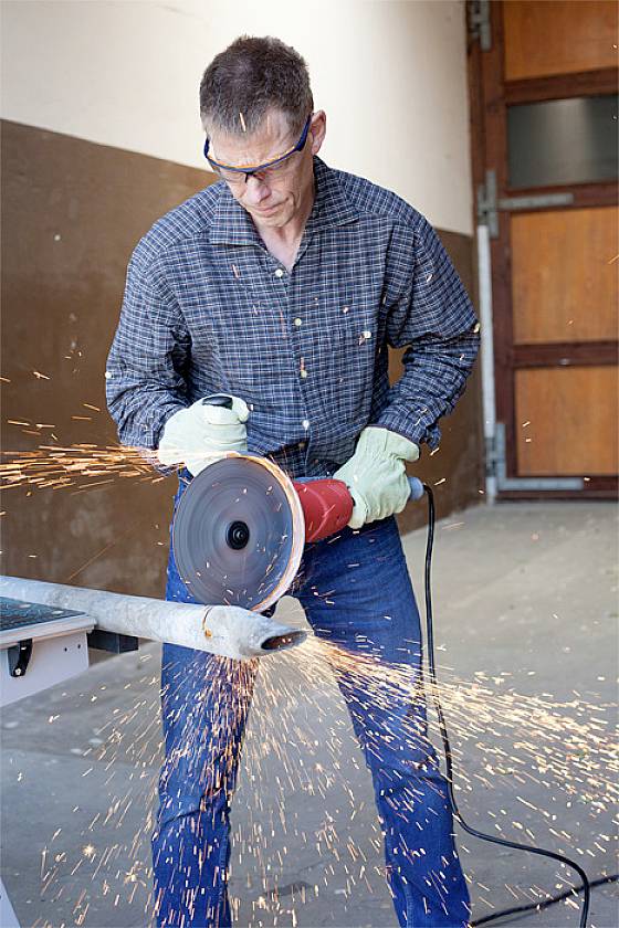 A person is cutting a metal pipe with an angle grinder. Sparks are flying, and they are wearing safety glasses and gloves.