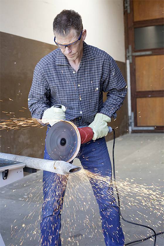 A man is grinding a metal pipe with a grinding machine. Sparks are flying. He is wearing safety glasses and gloves for protection.