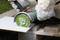 A person is cutting a white tile using an angle grinder. They are wearing safety gloves and cutting on a wooden surface.