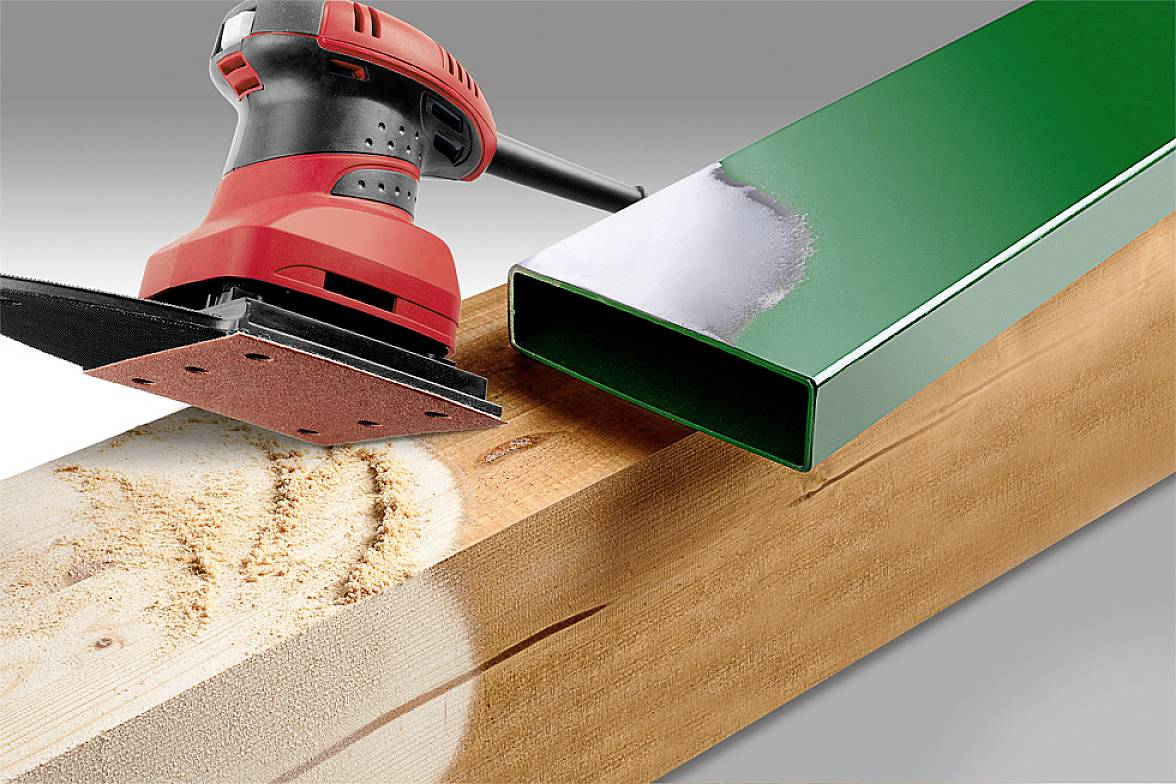 A red grinding machine on a wooden board with a green metal pipe beside it. The wood shows signs of grinding marks.