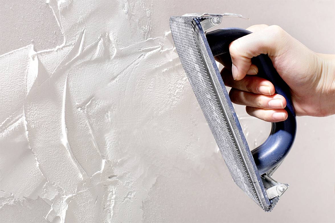 A hand smooths a wall with a trowel and white plaster to create an even surface.