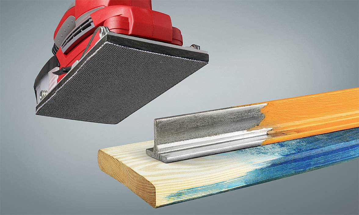 An electric sanding tool hovers over a partially sanded wooden board and a metallic angle profile, used for removing paint.