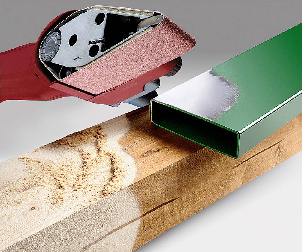 A red belt sander smooths a wooden surface. Beside it, a green metal profile lies on the wood, illustrating the sanding process.
