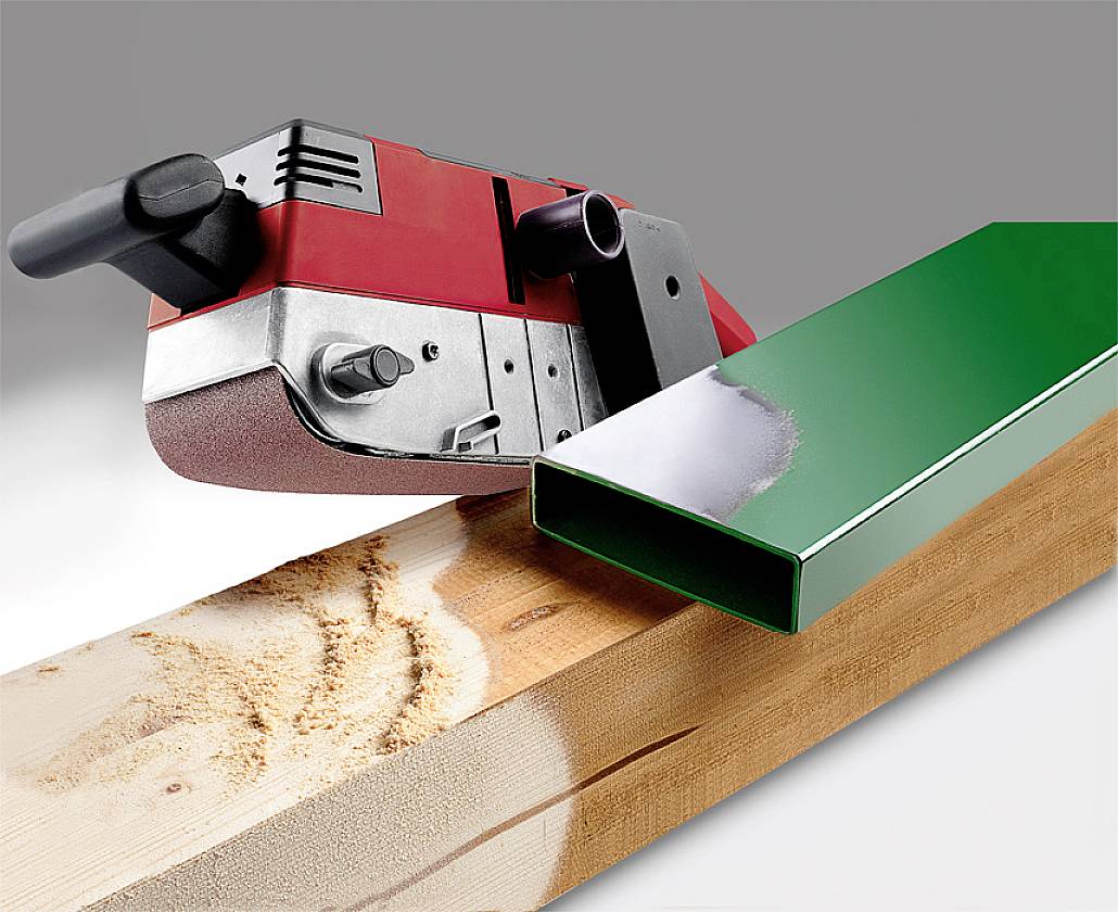 A bright red grinding tool is sanding a piece of wood next to a smooth, green metal pipe.