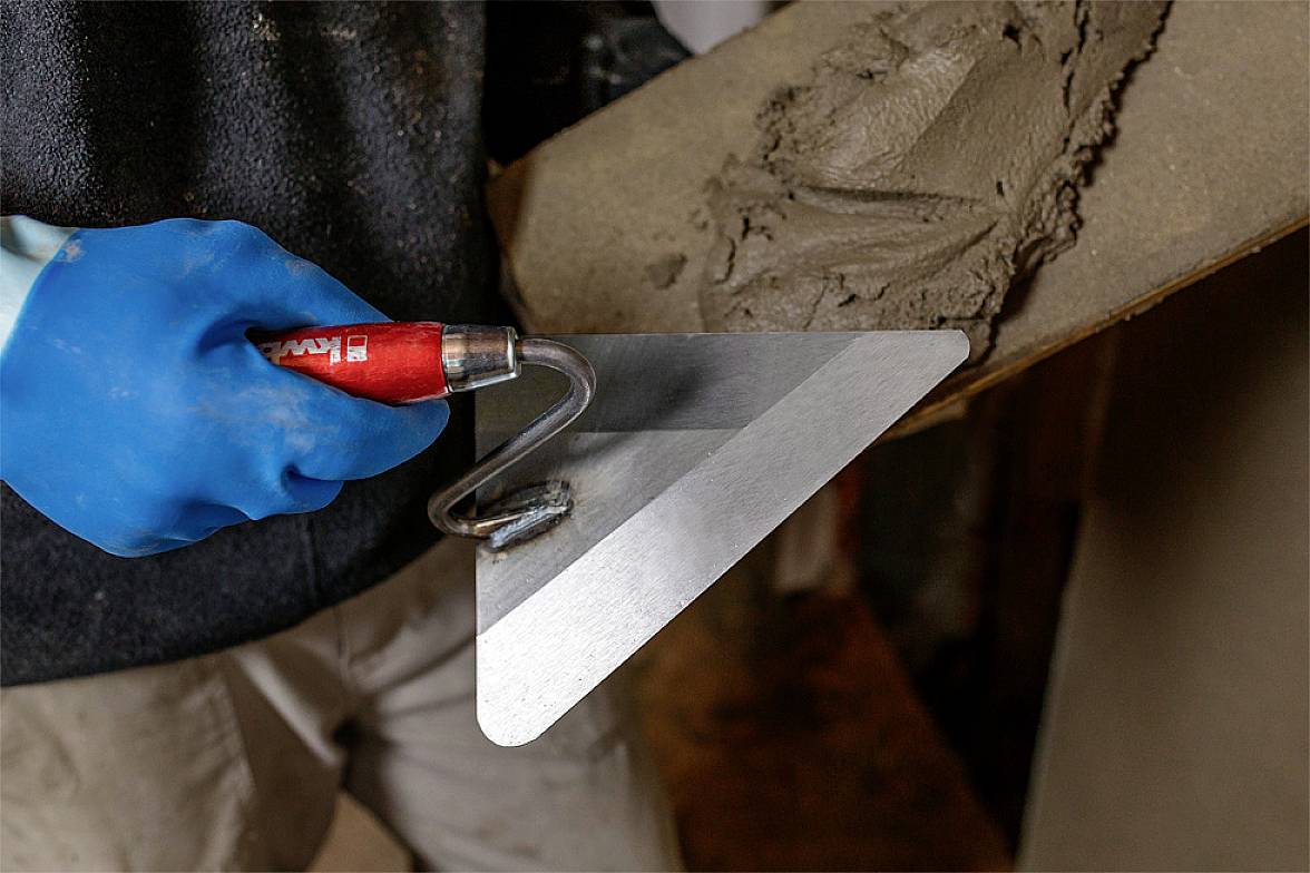 A person is wearing blue gloves and holding a trowel, using it to apply cement to another trowel.