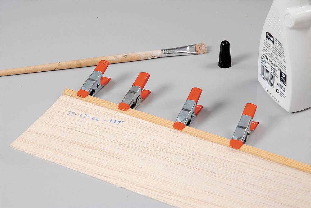 Wooden board secured with clamps, taped, and prepared with glue, brush, and lid against a grey background. Woodworking tools.