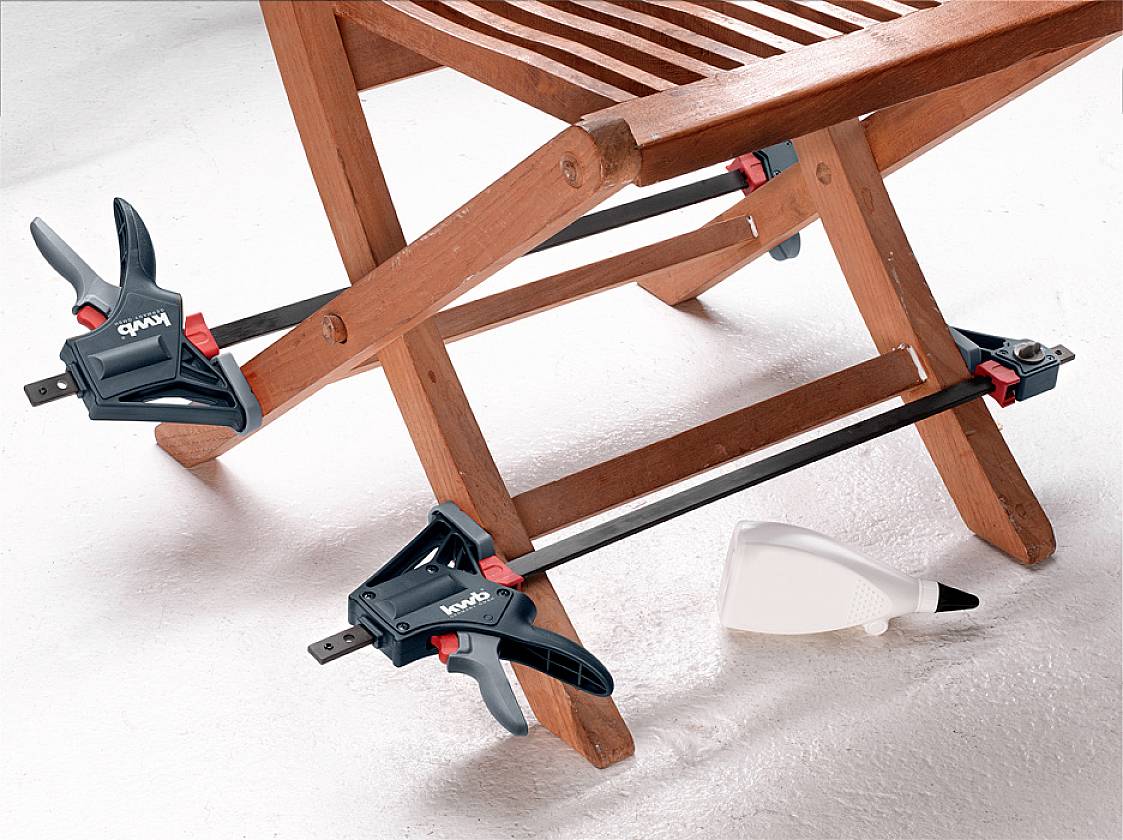 A wooden bench is secured with two black clamps to carry out repair work. A glue container is lying beside it.