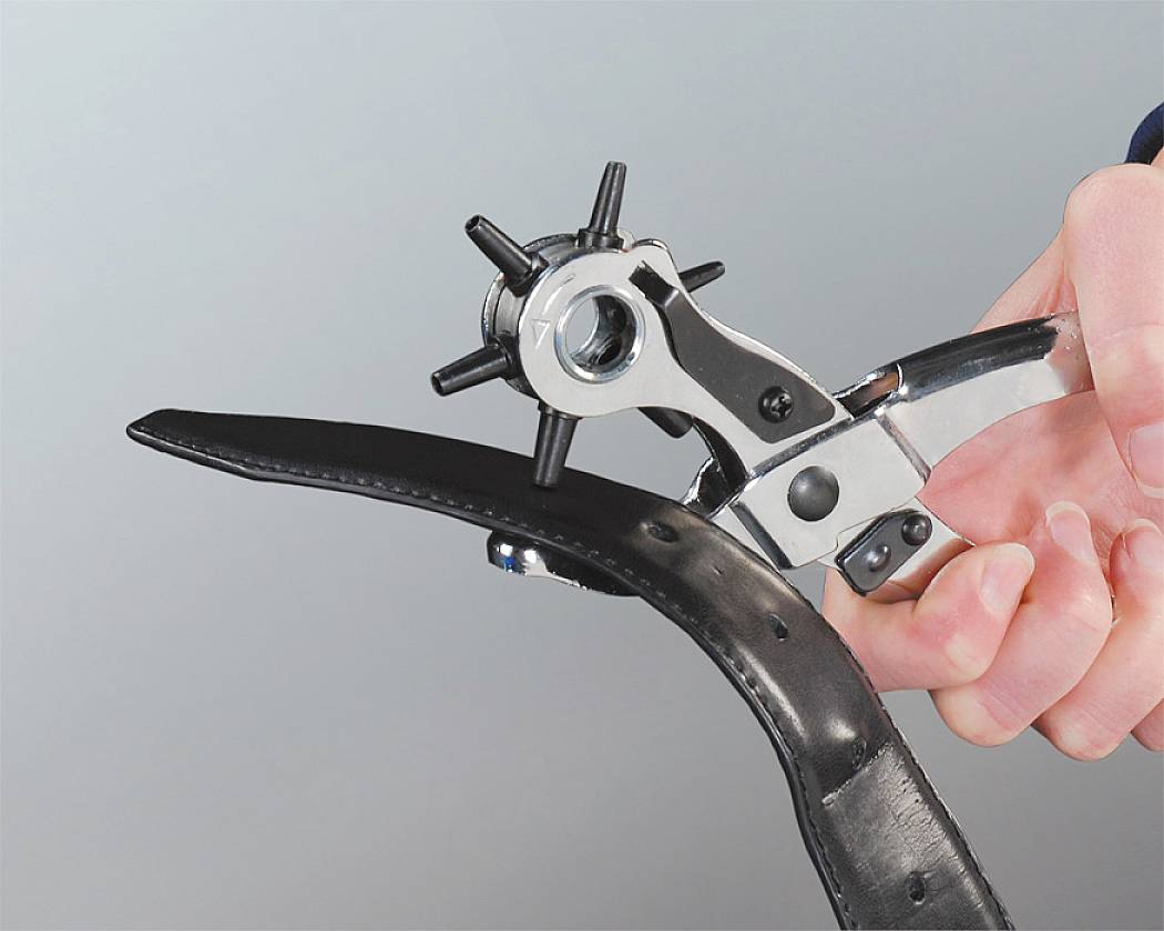 A hand holds a hole punch, creating an additional hole in a black leather belt.