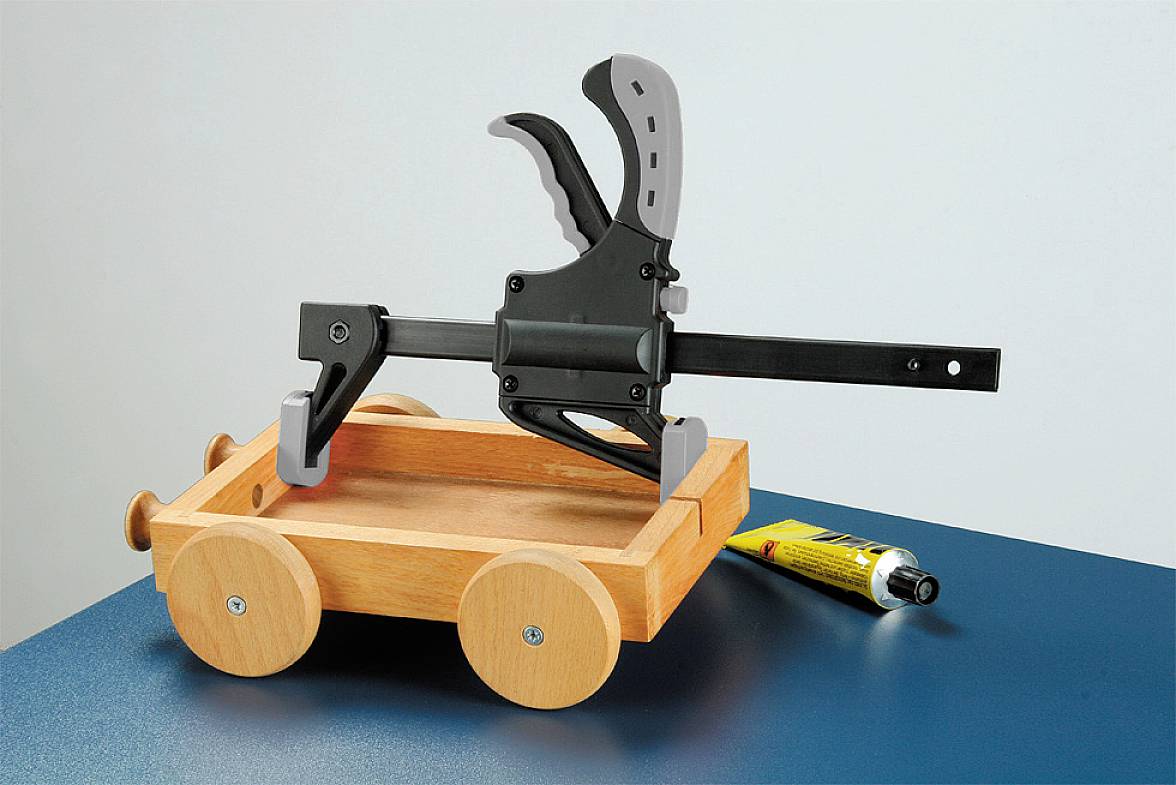 Wooden cart on a table with a G-clamp on top; a yellow tube of adhesive lies beside it.