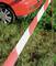 Red car parked next to a red and white barrier on a grassy area.