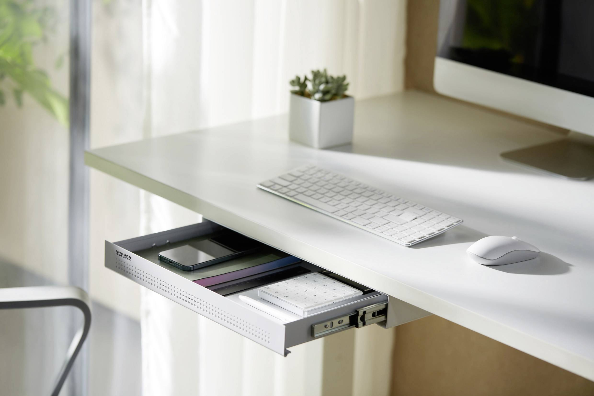A white desk with an open drawer containing pens and notebooks. A keyboard, mouse, and small plant pot are placed on the table.