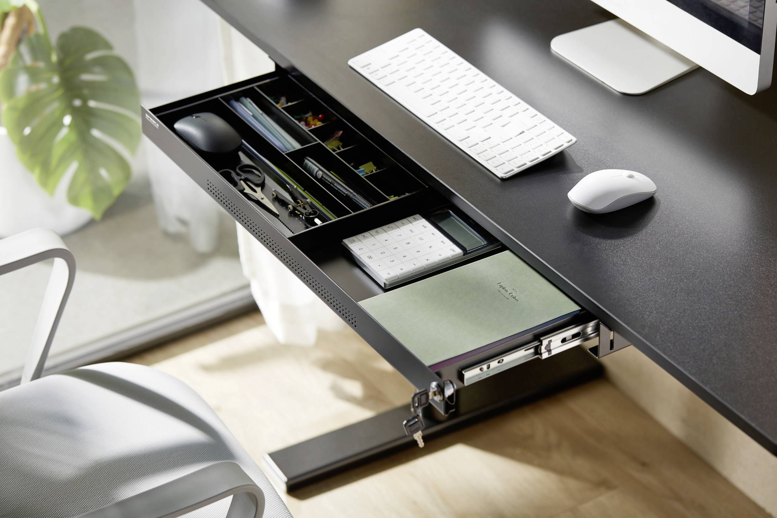 A modern desk with an extended drawer reveals an organised arrangement of office supplies, including a mouse, calculator, and notebook.