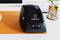 A black label printer by the brand Renkforce sits on an orange background, next to a decoration of cinnamon and lemon.