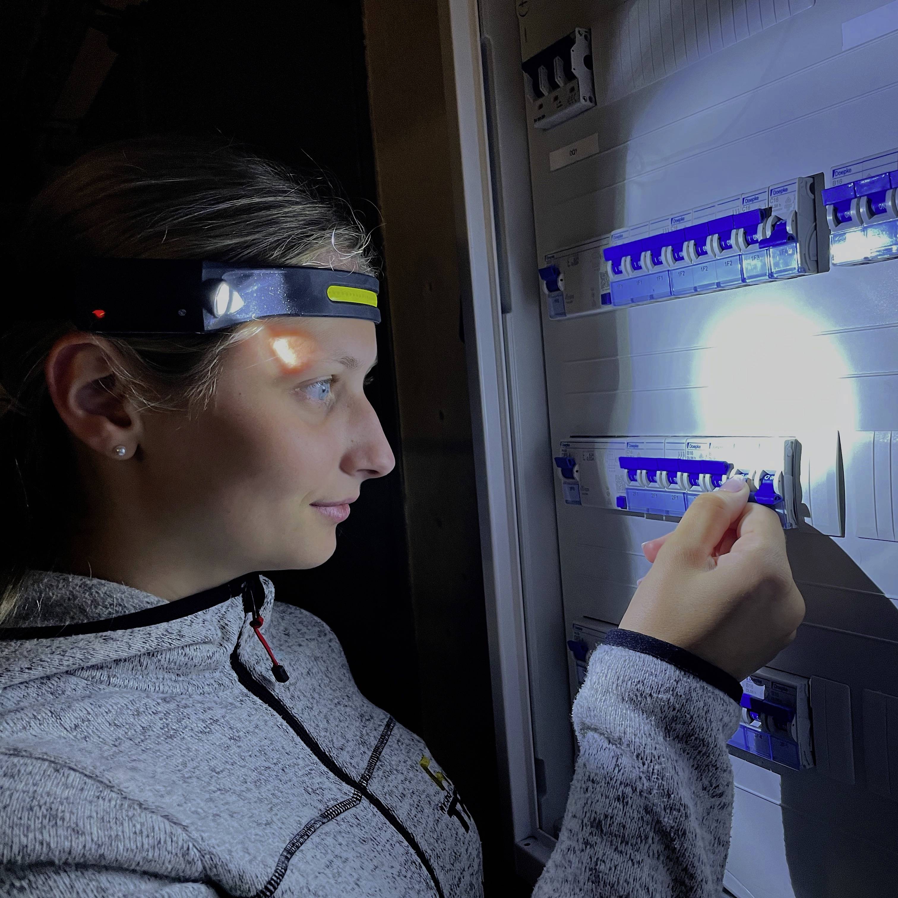 A person is wearing a head torch in a dark room and switching on a circuit breaker in an electrical panel.