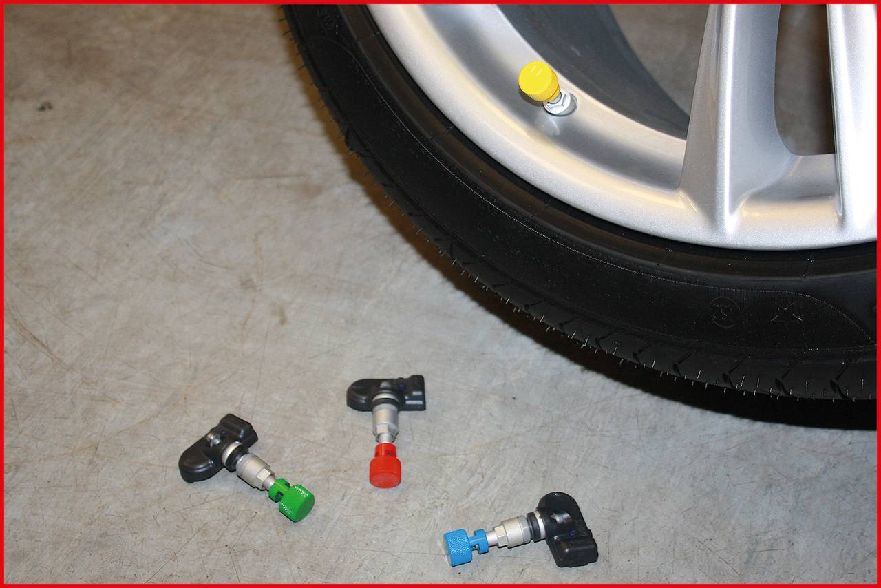 A car tyre with a yellow valve; three coloured valves for the tyre pressure sensor are lying beside it on the ground.