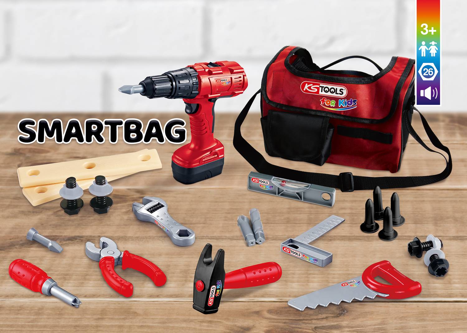 A set of toy tools: red cordless drill, tool bag, spanner, saw and additional accessories on a wooden table.